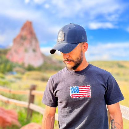 Man wearing a cap and t-shirt with an American flag in a scenic outdoor setting