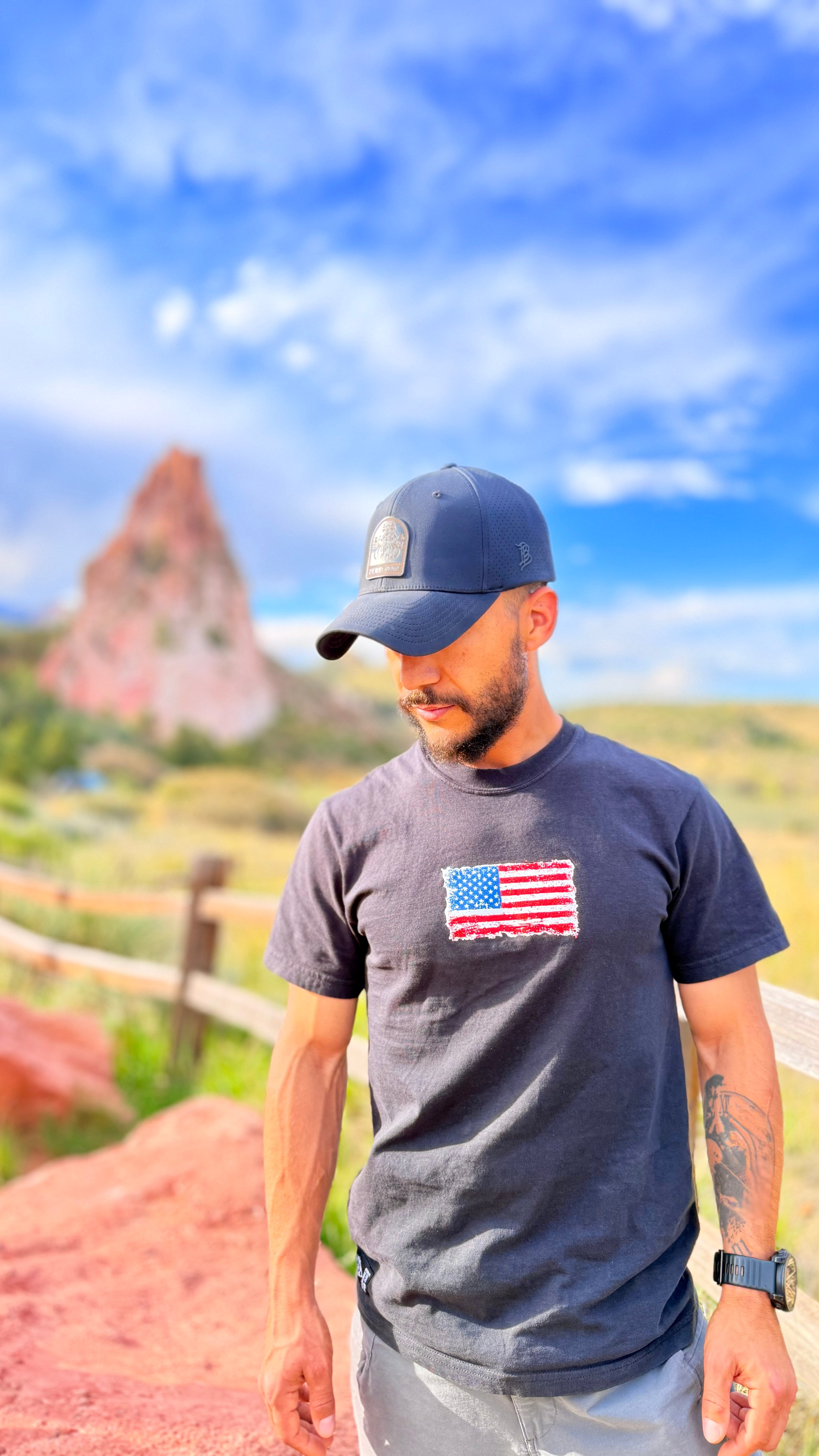 Man wearing a cap and t-shirt with an American flag in a scenic outdoor setting