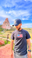 Man wearing a cap and t-shirt with an American flag in a scenic outdoor setting